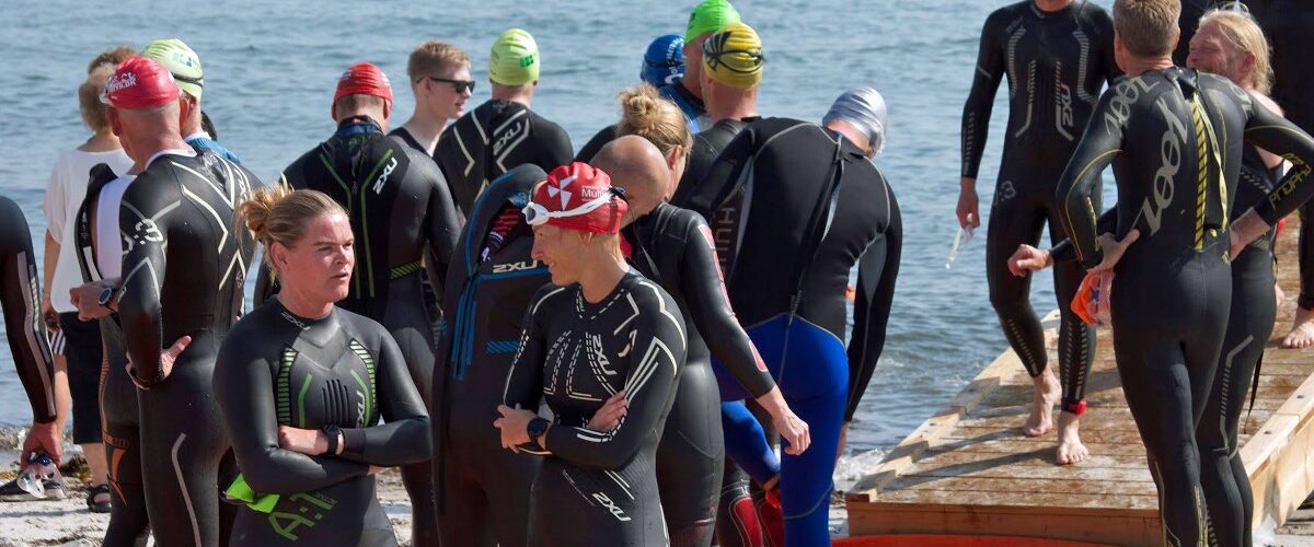 Atleter i våddragt i venteposition på stranden før stævnestart